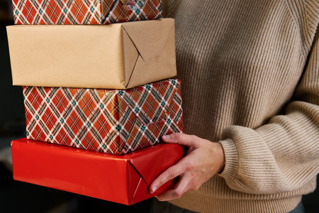 Woman prepares gifts for friends and relatives on Christmas eve. Woman holds pile of presents in gift boxes wrapping in craft paperの写真素材