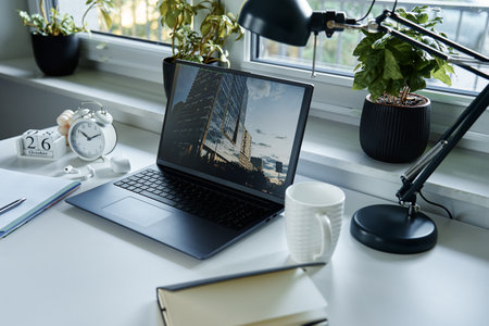 Home office workplace. Table with laptop, notebook and hot coffee near window in living room.の写真素材