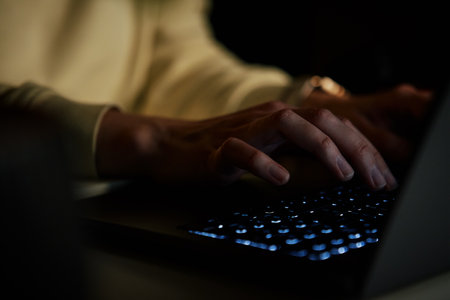 Close up shot of anonymous woman typing on laptop keyboard at night. Online communication and working after hours conceptの写真素材