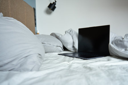 Opened laptop in unmade bed with pillows and crumpled bedsheets at morning. Comfortable workplace for freelancer, work from homeの写真素材