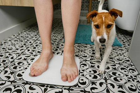 Bare feet woman checking her weight on weighing scales in bathroom. Female measuring her weight...