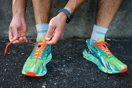 Athletic man tying his running shoes before exercising. Male runner wearing Asics Noosa Tri 13 at stadium track preparing to running. Katy Wroclawskie, Poland - June 10, 2023のeditorial素材