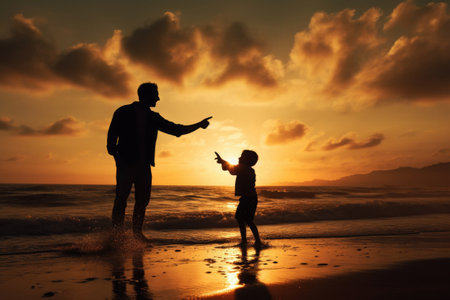 Father and son silhouettes walking at sunset beach together. Happy relationships in familyの素材