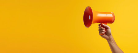 Hand holds megaphone on yellow background with copy space. Banner with loudspeaker for advertising adsの素材