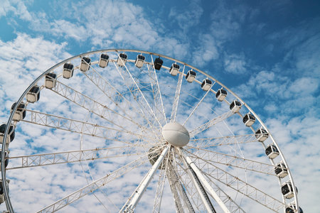 Ferris wheel rotates against background of blue cloudy sky. Amusement park attraction. Summer holidaysの写真素材