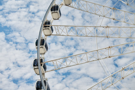 Ferris wheel rotates against background of blue cloudy sky. Amusement park attraction. Summer holidaysの写真素材
