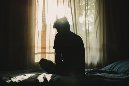Silhouette of depressed man sitting on bed in front of window, Sleep problems due to stress, mental disorderの素材