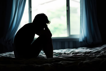 Silhouette of depressed man sitting on bed in front of window, Sleep problems due to stress, mental disorderの素材
