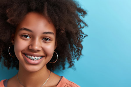 Smiling african american girl with dental braces on blue background, Orthodontic treatment, Teenager teeth correctionの素材