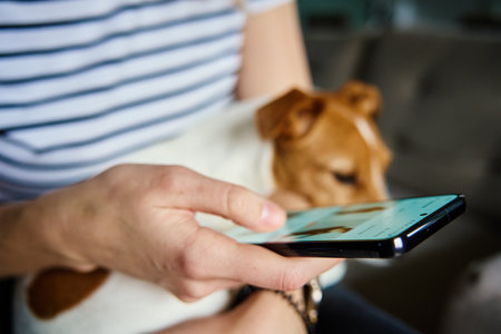 Woman using mobile phone at home. Female sitting on sofa with dog and browsing social networks on...