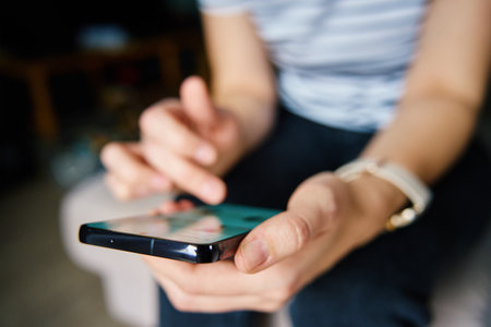 Close-up person casually using smartphone with social media feed displayed on screen, suggesting...