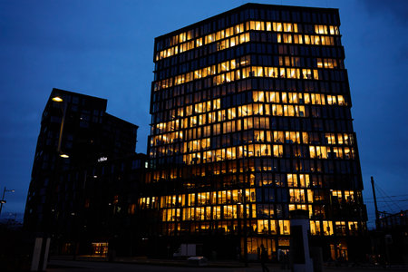 Office building lights up the evening with windows glowing in the dusk, showcasing urban work life after hoursの写真素材