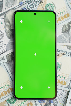 Smartphone with green screen on pile of dollar banknotes, top view. Concept of online earningsの写真素材