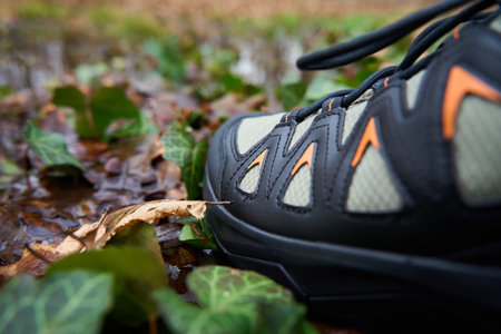 Hiking boots stands on forest floor, submerged in water puddle, surrounded by fallen leaves. Sturdy...