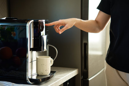 Woman preparing fresh cup of coffee with modern espresso machine. Female hand pressing button on...