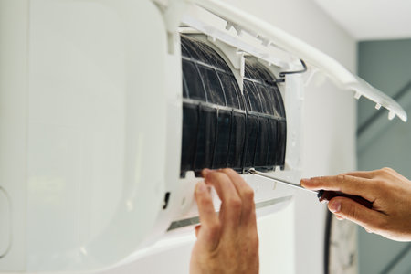 Air conditioner maintenance. Male technician repairs home climate system in living room. Man is cleaning filters of conditionerの写真素材