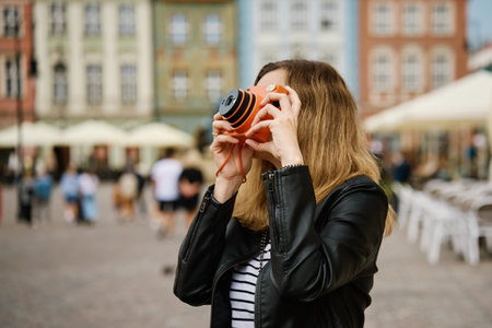 Woman taking picture using orange instant camera. Tourist captures memories during travel with...