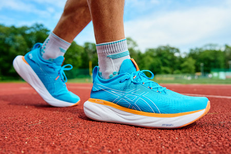Athlete wearing blue Asics Gel-Nimbus 25 running shoes on red stadium track during training. Sportsman legs in sport sneakers at racetrack. Katy Wroclawskie, Poland - May 11, 2024のeditorial素材