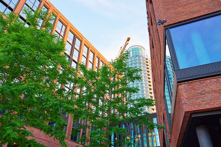 Modern urban architecture with brick buildings, lush green trees and glass sky bridge connecting...