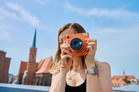 Woman taking photos in European city surrounded by colorful historic buildings. Female tourist captures memories during travel with vintage instant cameraの写真素材