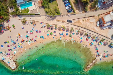 Sea beach with colorful umbrellas and relaxing people, aerial top view. Crowded sandy beach at high season. Tourists at summer holidays in Croatiaの写真素材