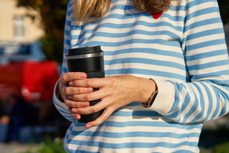 Woman holding black reusable coffee cup outdoors. Concept of eco-friendly lifestyle