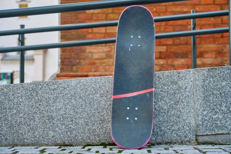 Used scratched pink skateboard against stone wall at city street. Urban sport and youth subculture...
