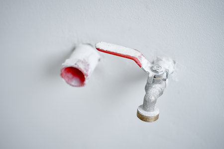 Close-up of water faucet with red handle protruding from white wall in empty apartment. Plumbing work during home renovationの写真素材