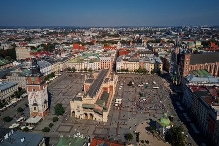 Aerial view of Krakow main market square with historic Cloth Hall (Sukiennice) surrounding colorful buildings on sunny day. Cityscape of Krakow in Poland with tourists walking in old townの写真素材