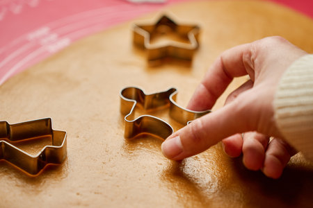 Woman using cookie cutters to shape gingerbread dough on red mat. Baking traditional Christmas cookies in home kitchenの写真素材
