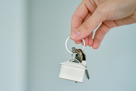 Close up hand holding keys with house shaped keychain in front of blurred new apartment interior....