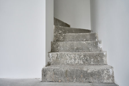Empty apartment with unfinished concrete staircase and white walls undergoing renovation. Interior of building under constructionの写真素材