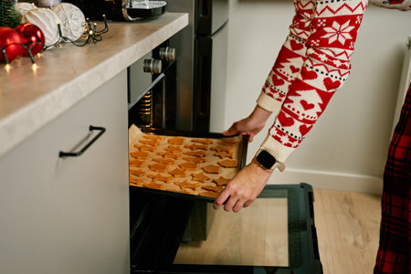 Woman in red festive sweater putting tray of Christmas cookies into oven. Process of cooking...