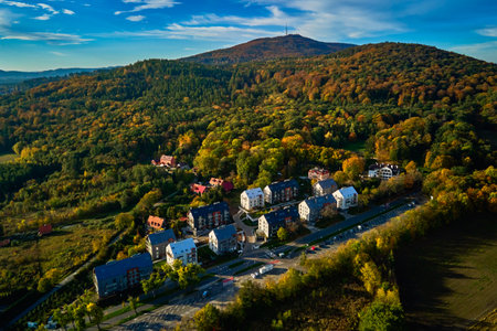 Modern residential buildings near vibrant autumn forest, aerial view. Contemporary apartments in suburban eco friendly neighborhood with green spaces near mountains in small European townの写真素材