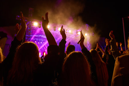 Silhouettes of crowd at concert in front of stage with bright spotlights. People enjoy live music at the bands performance. Concert hall with musicians on stage and fans during music festivalの写真素材