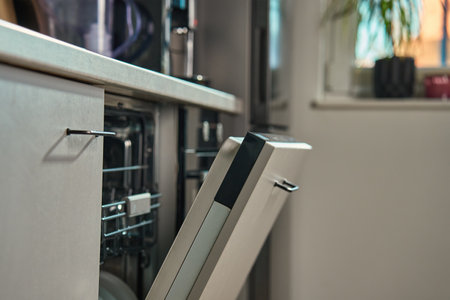 Partially open dishwasher integrated into modern kitchen with natural light. Energy-efficient home appliance for convenient dish cleaningの写真素材