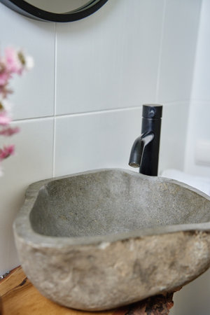 Natural stone sink with black faucet and floral decor with dried flowers on wooden countertop in small bathroom. Stylish bathroom interior in modern apartmentの写真素材