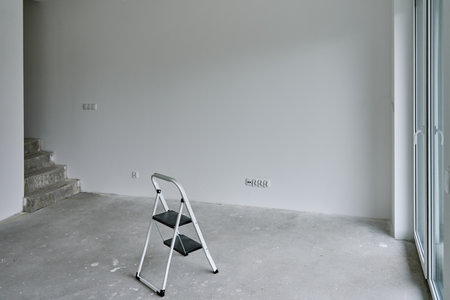 Empty room under renovation with bare concrete flooring, white painted walls, small step ladder and...