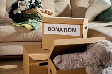 Donation boxes filled with clothes and stuffed toy on couch. Charity and community aid concept