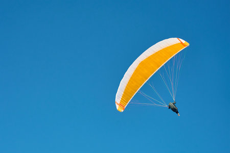 Person is flying on paraglider against blue sky. Paraglide with yellow canopy.
