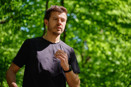 Man running on trail through green park in summer day. Outdoor cardio training in nature. Male runner jogging on forest path. Wellness and active lifestyle conceptの写真素材