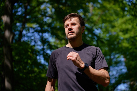 Man running on trail through green park in summer day. Outdoor cardio training in nature. Male runner jogging on forest path. Wellness and active lifestyle conceptの写真素材