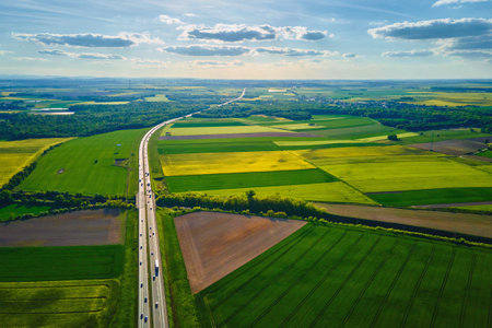 Aerial view of highway cutting through agricultural fields with blooming rapeseed crops....