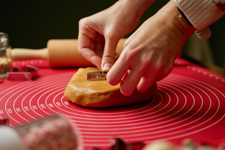 Woman using cookie cutters to shape gingerbread dough on red mat. Baking traditional Christmas cookies in home kitchenの写真素材
