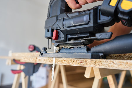 Close up of electrical handheld jigsaw cutting wooden board in workshop. Work tools for manual labor. Carpentry and woodworking conceptの写真素材