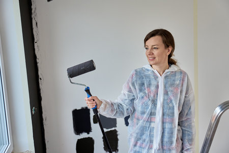 Woman holding roller brush while painting wall during apartment renovation. Concept of gender equality and women in constructionの写真素材