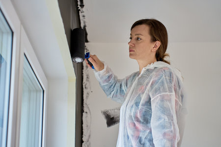 Woman painting white wall in black color using paint roller in modern apartment. Home renovation process, redecoration and interior design updatingの写真素材