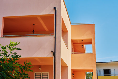 Modern building with pastel peach walls and open balconies under clear blue sky. Mediterranean residential architecture, vacation house and urban lifestyleの写真素材