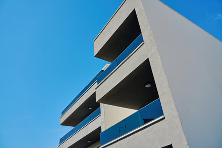 Facade of modern apartment building with minimalist balconies and glass railing under blue sky. Contemporary residential architecture, geometric design and urban housing conceptの写真素材