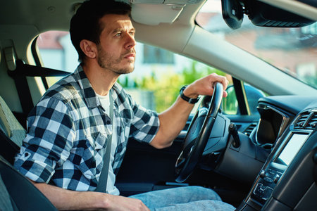 Man behind the wheel looks attentively at rear view mirror while driving car. Focus, safety awareness and responsible driving conceptの写真素材